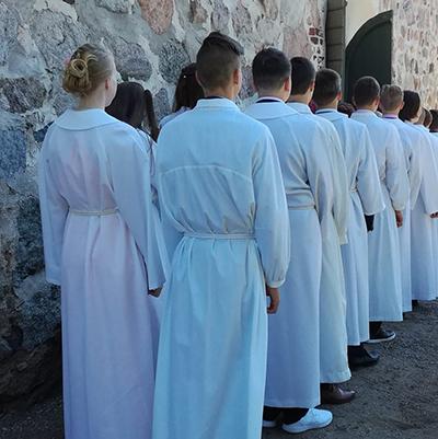 Rippikoululaisia jonossa valmistautumassa konfirmaatioon albat yllään.